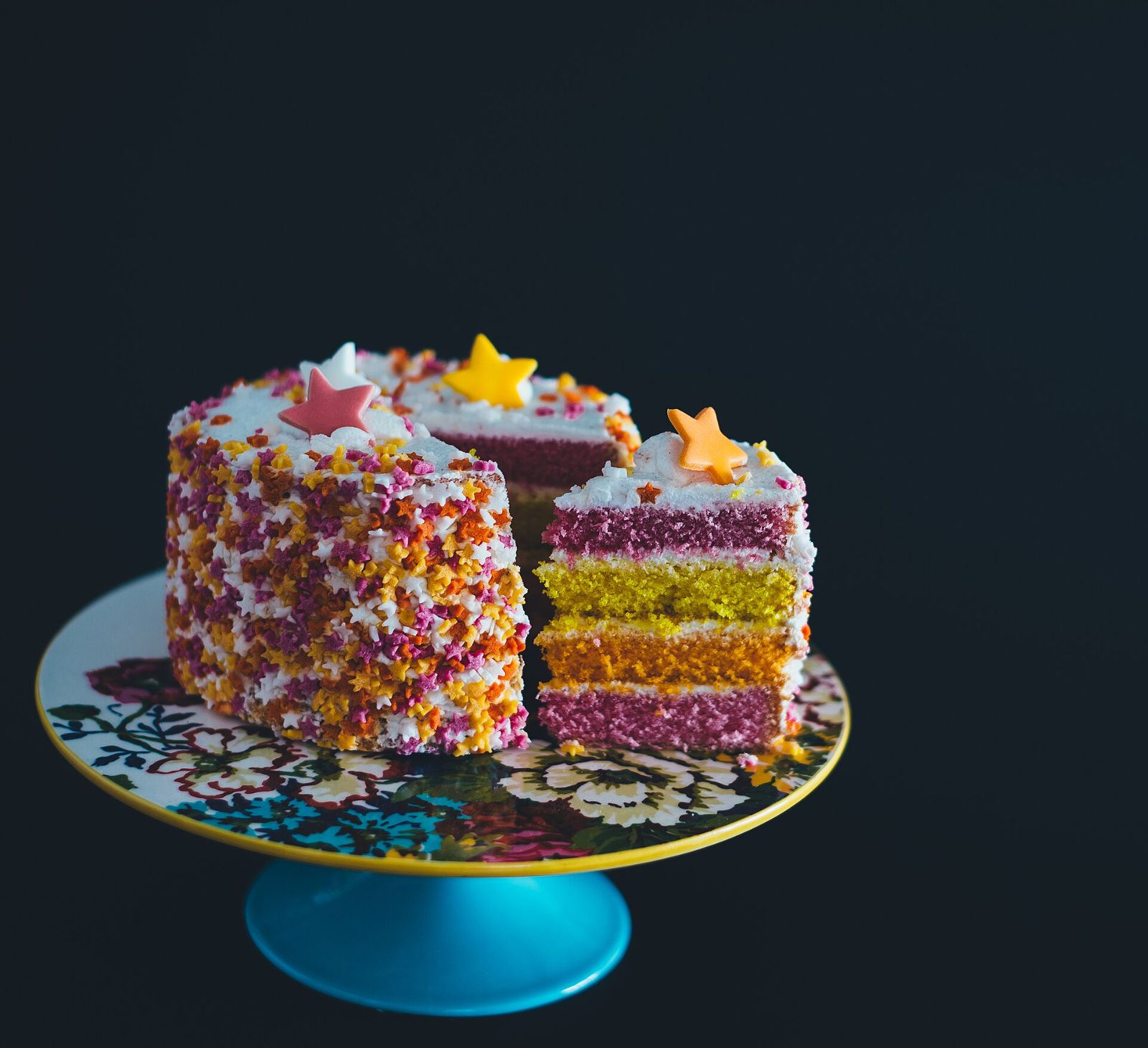 A colourful layered cake with sprinkles and stars on a cake stand
